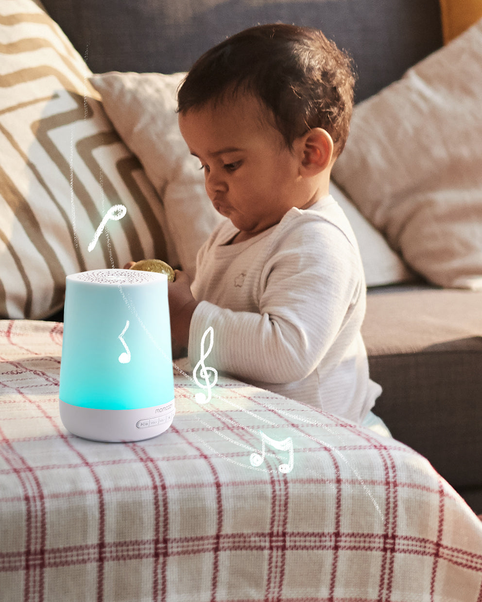 A baby looks at a blue and white smart sound machine with musical notes floating around it.