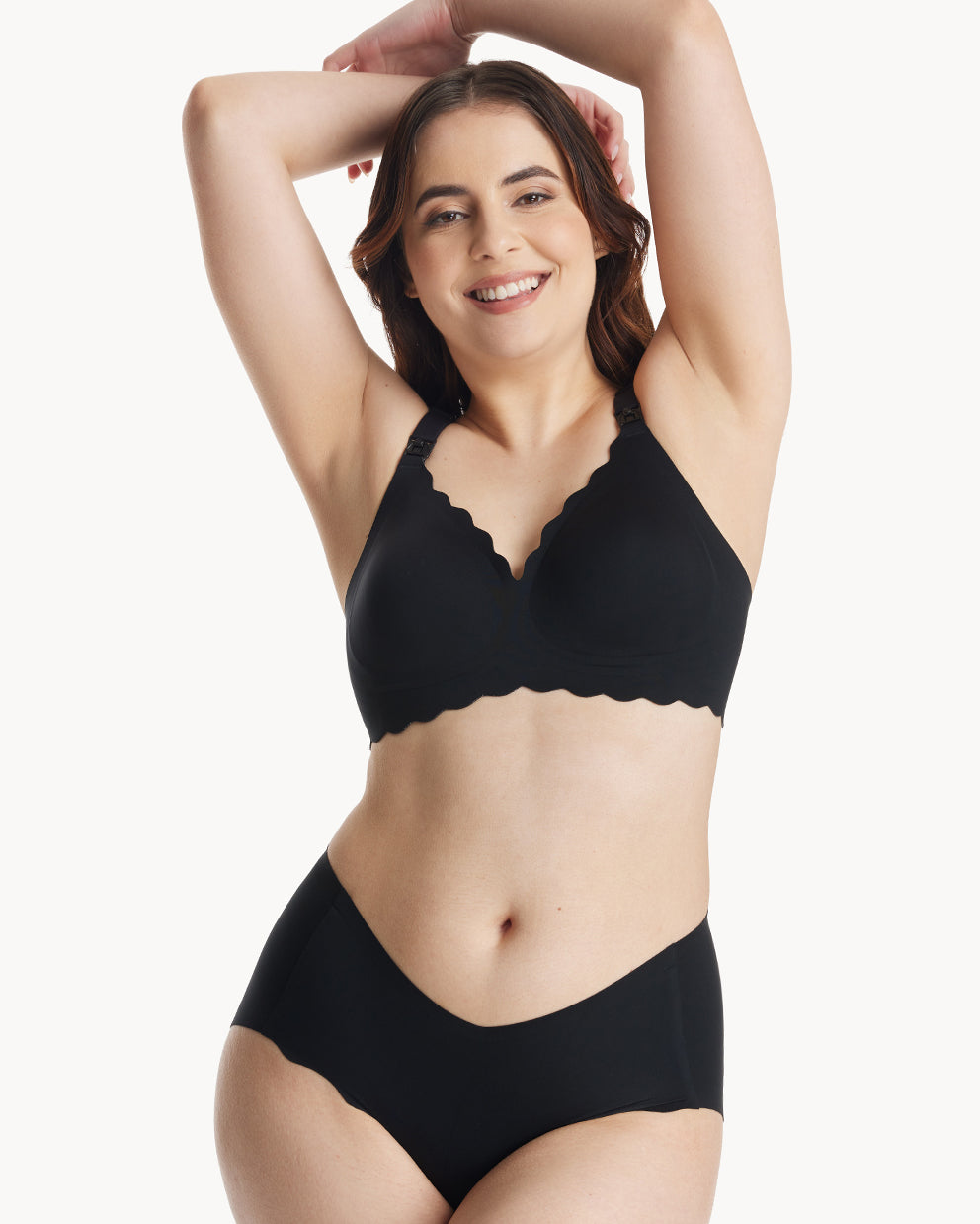 Smiling woman wearing a black seamless nursing bra with scalloped design and matching seamless underwear.