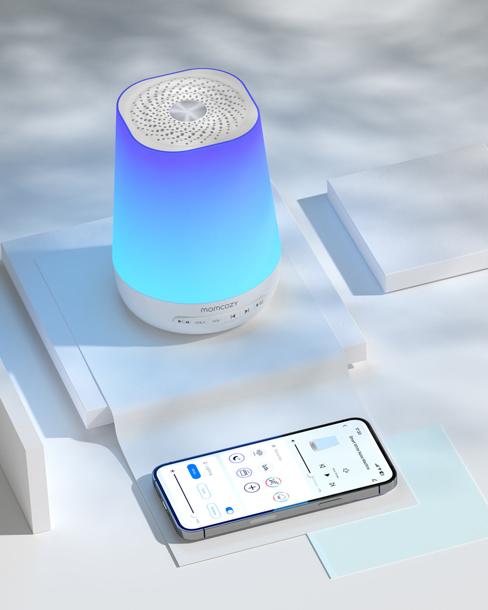 White smart baby sound machine with blue gradient light, controlled by a smartphone app showing sound machine interface.