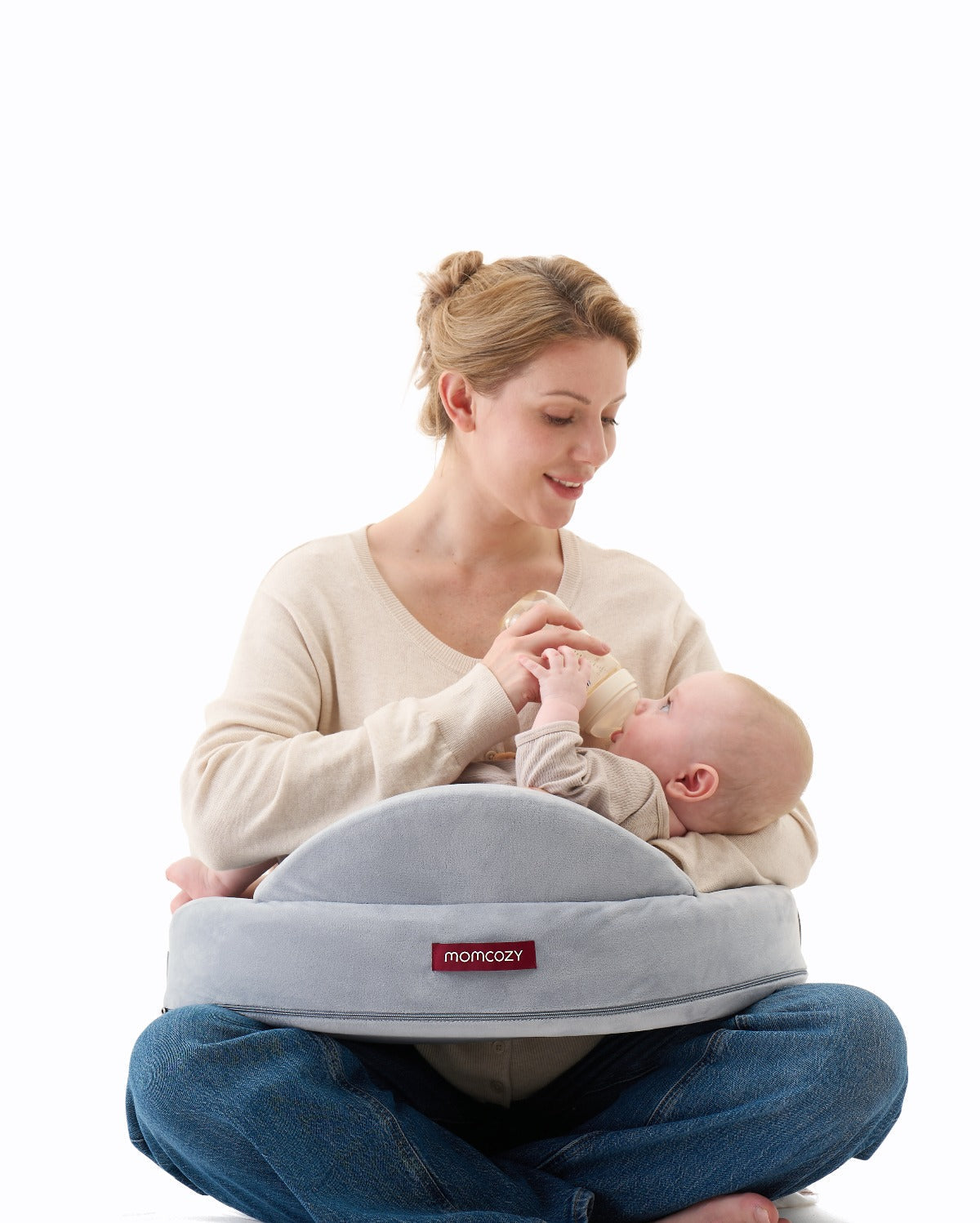 Grey Momcozy MaxSupport nursing pillow supporting baby while mother bottle feeds.