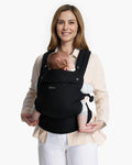 Momcozy PureHug Baby Carrier. Black carrier, comfortable design, worn by mother holding baby. Ideal for babywearing.
