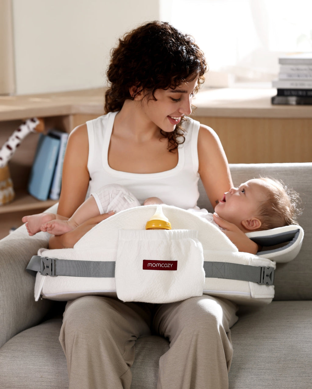 Momcozy memory foam nursing pillow supporting baby, white with bottle pocket.